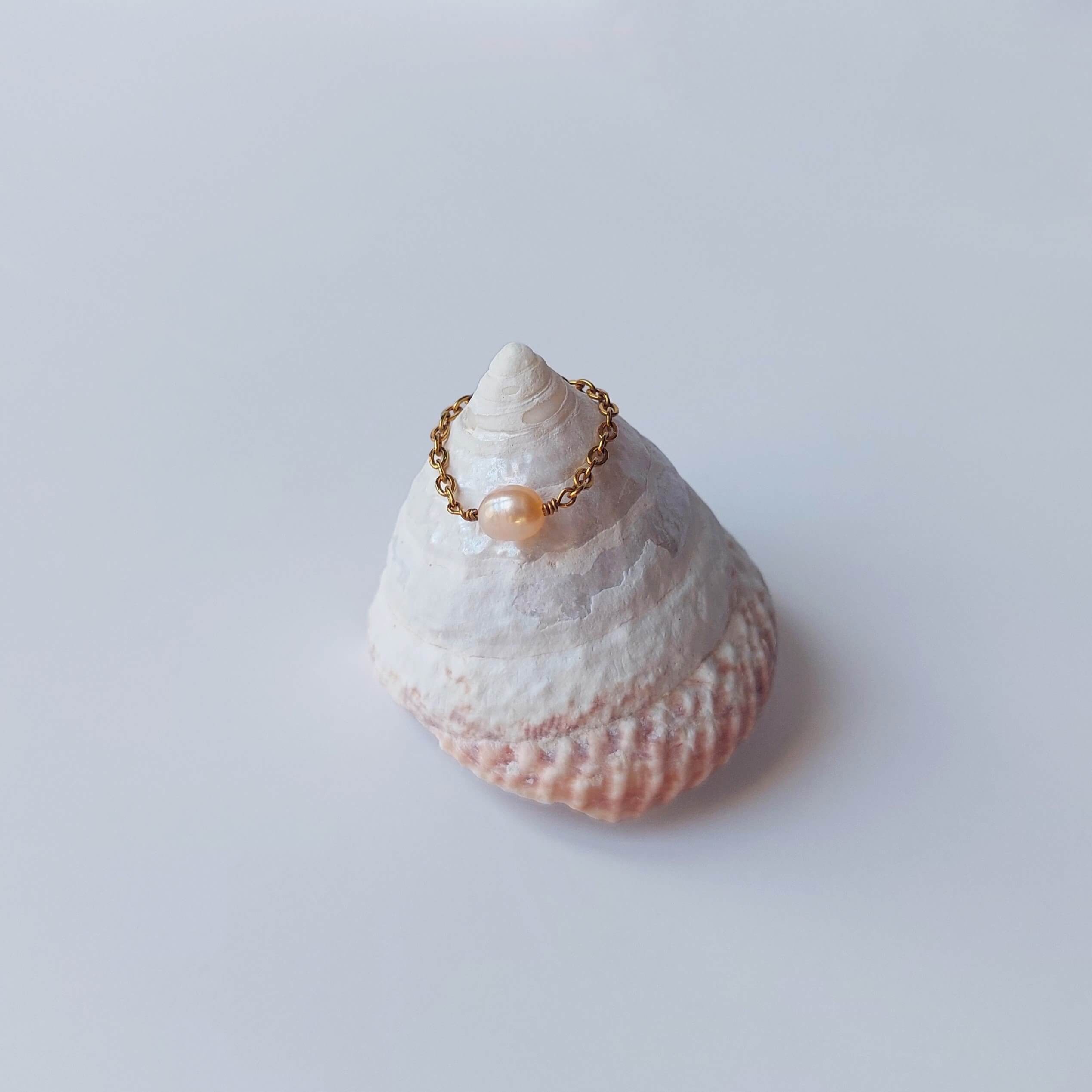 Bague faite d'une chaine fine en acier inoxydable doré et perle d'eau douce orange posée sur un coquillage
