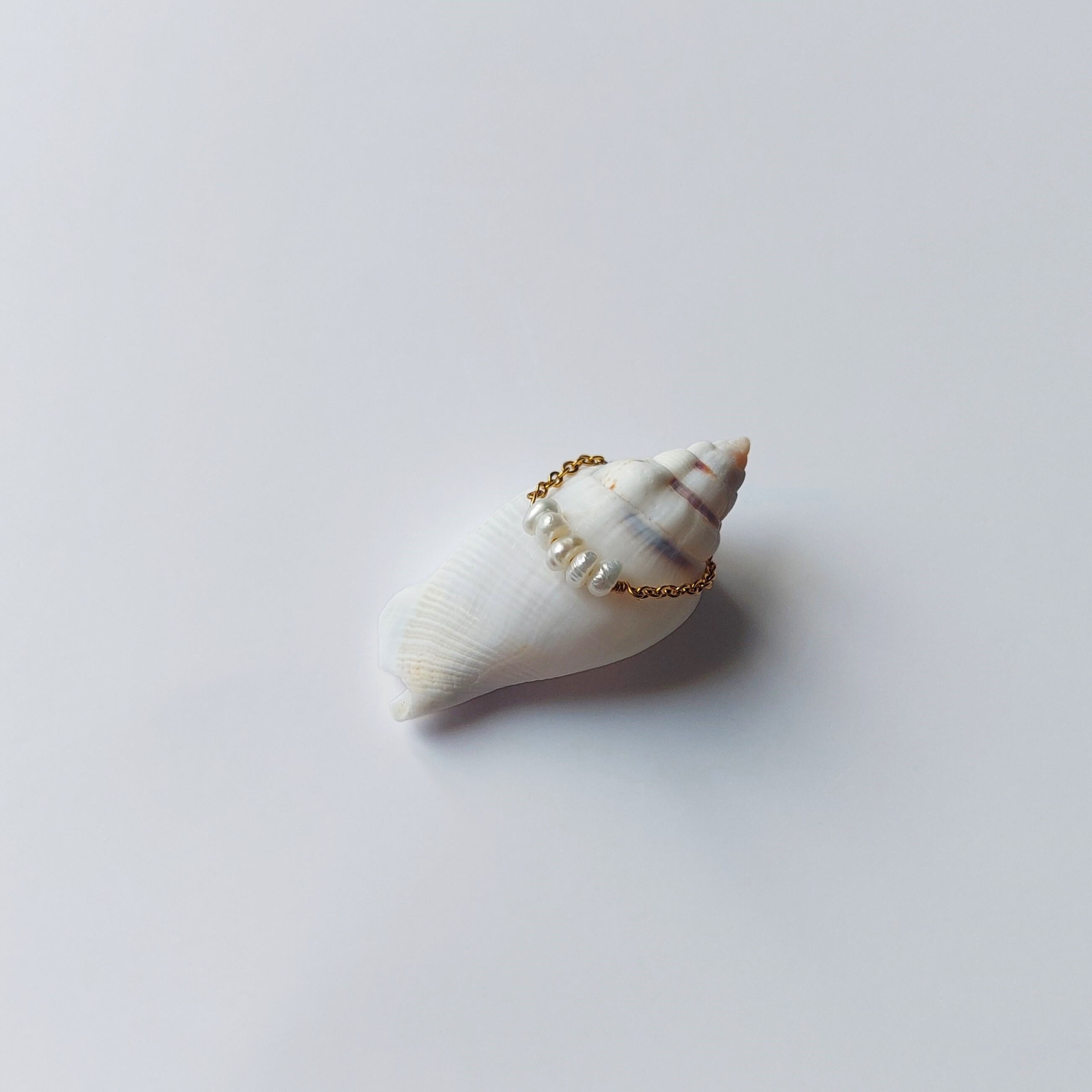 Bague faite en acier inoxydable doré et petites perles d'eau douce blanches posée sur un coquillage