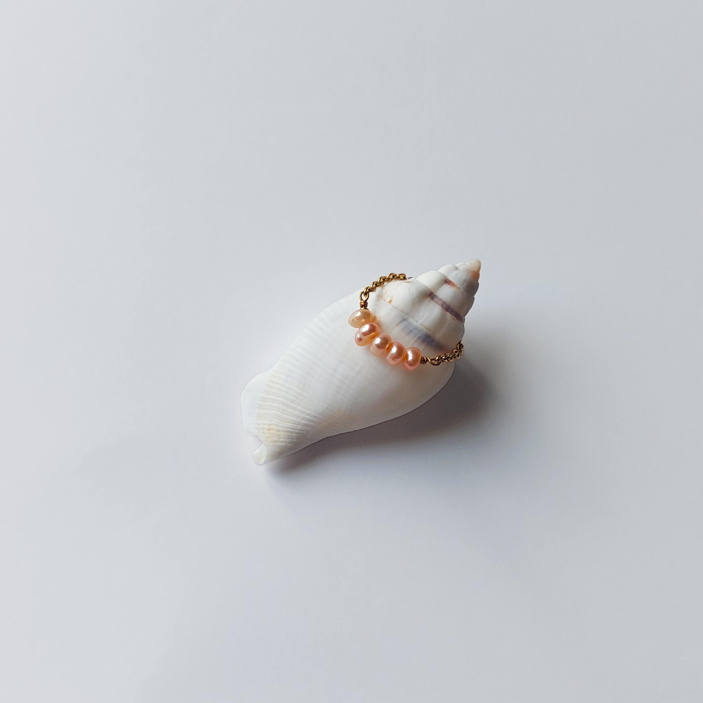 Bague faite en acier inoxydable doré et petites perles d'eau douce oranges posée sur un coquillage