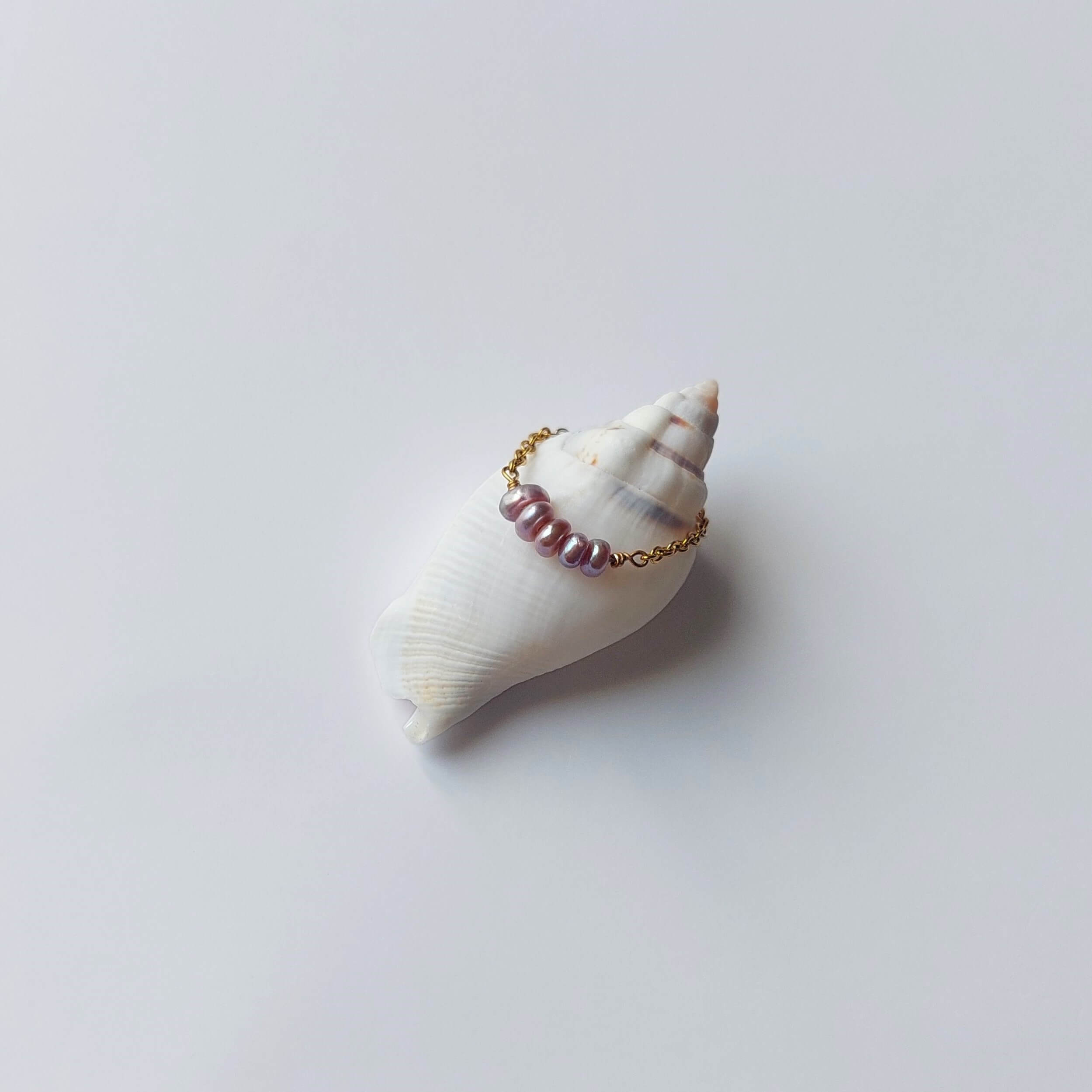 Bague faite en acier inoxydable doré et petites perles d'eau douce violettes posée sur un coquillage