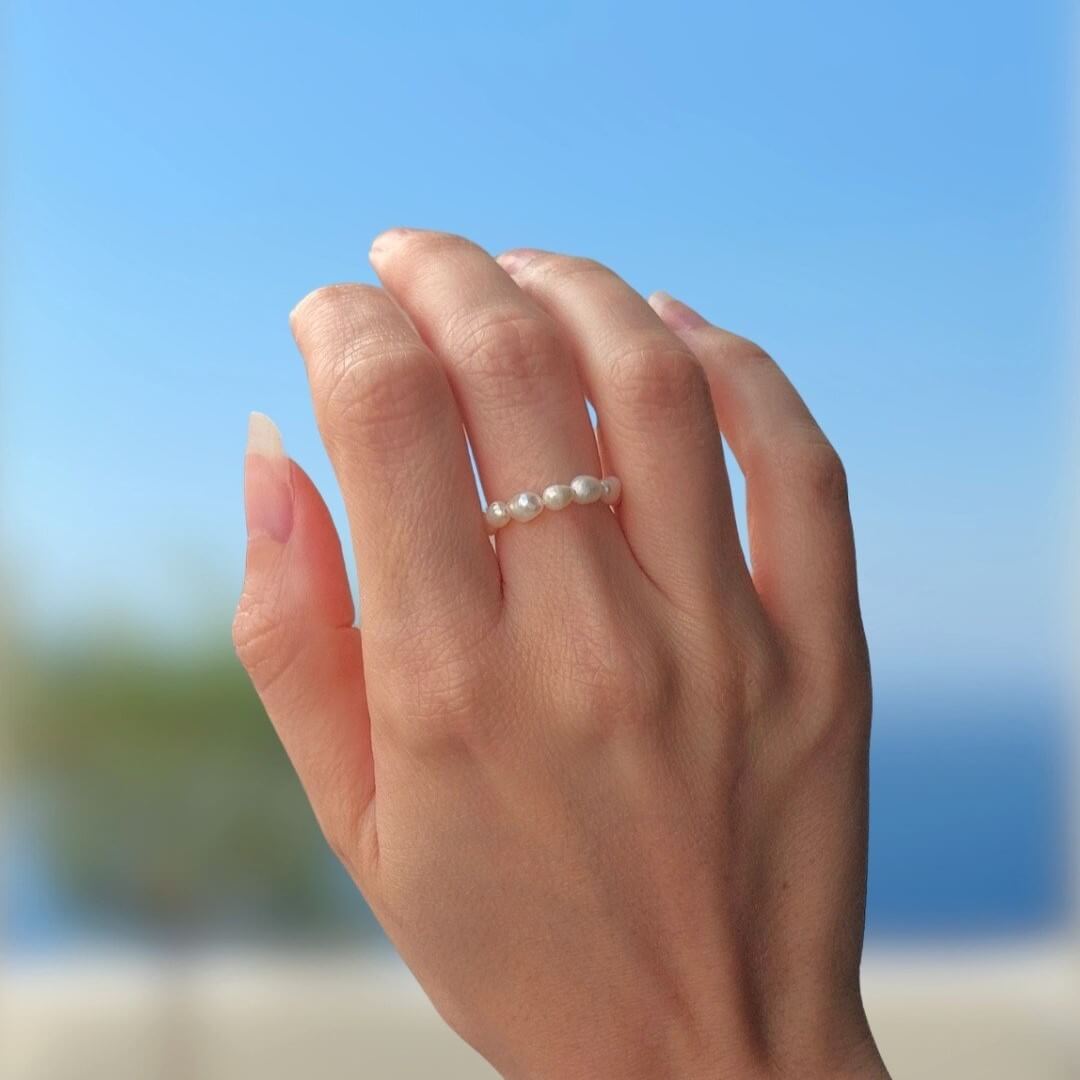 Bague portée, ornée de petites perles d'eau douce naturelles blanches, sur fond bleu. 