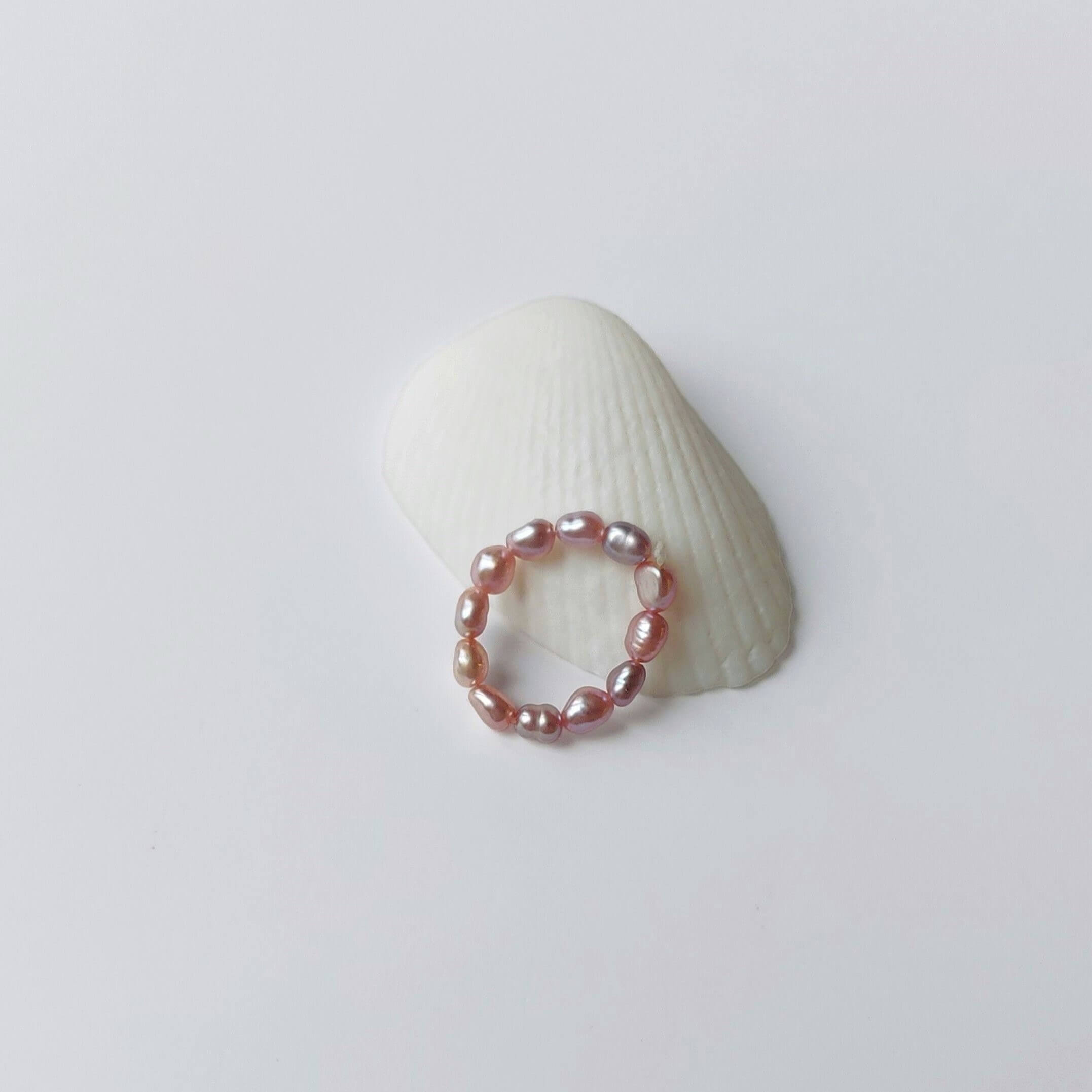Bague élastique faite uniquement de petites perles d'eau douce violettes posée sur un coquillage