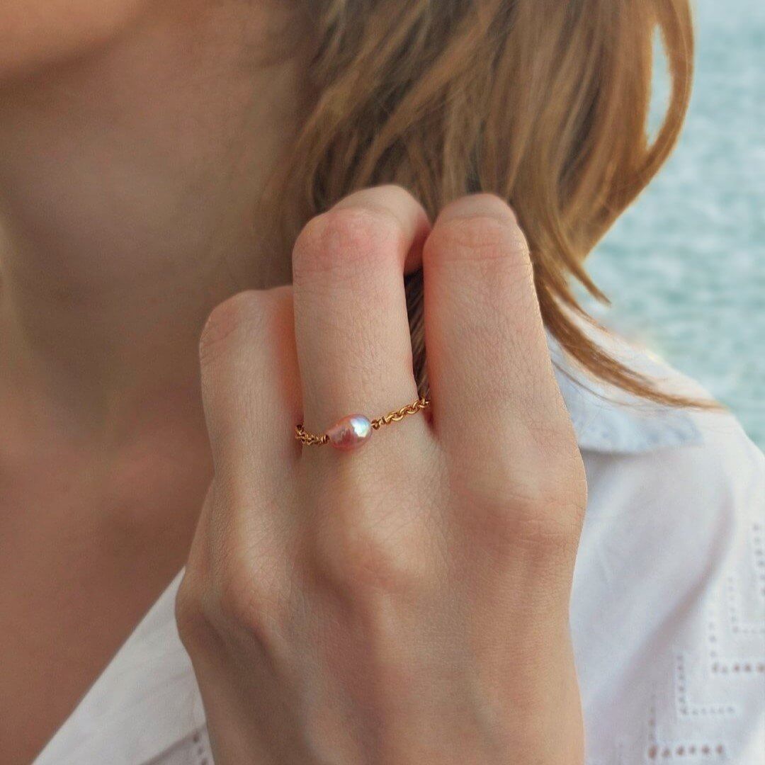 Bague portée, souple, avec une perle d'eau douce naturelle violette centrale. 