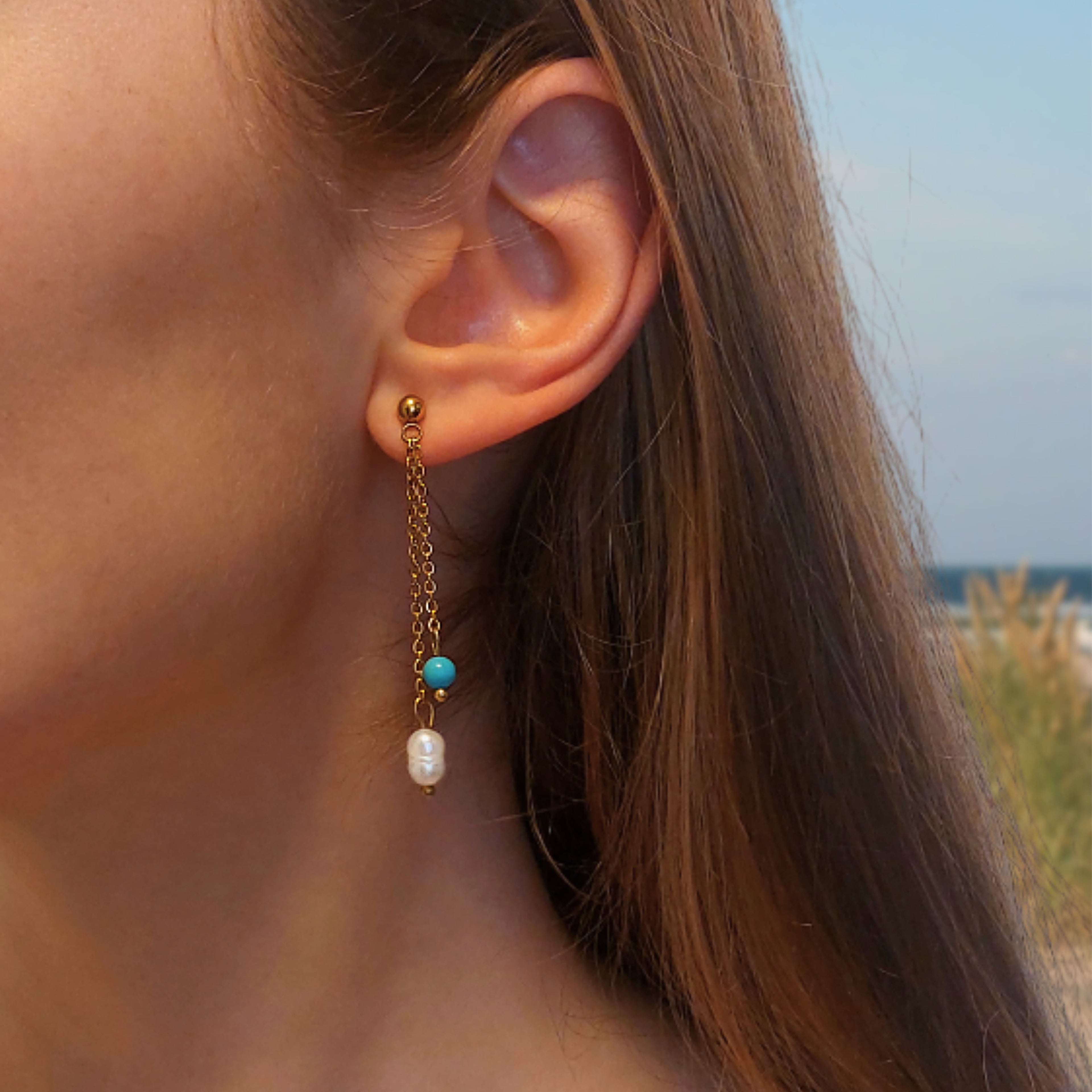 Boucles d'oreilles pendantes en acier inoxydable avec perles d'eau douce porté par une femme sur la plage. 