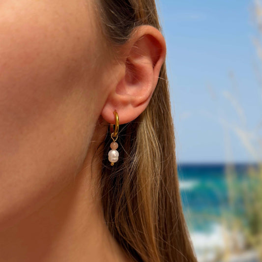 Boucles d'oreilles créoles en acier inoxydable avec perles d'eau douce porté par une femme sur la plage. 