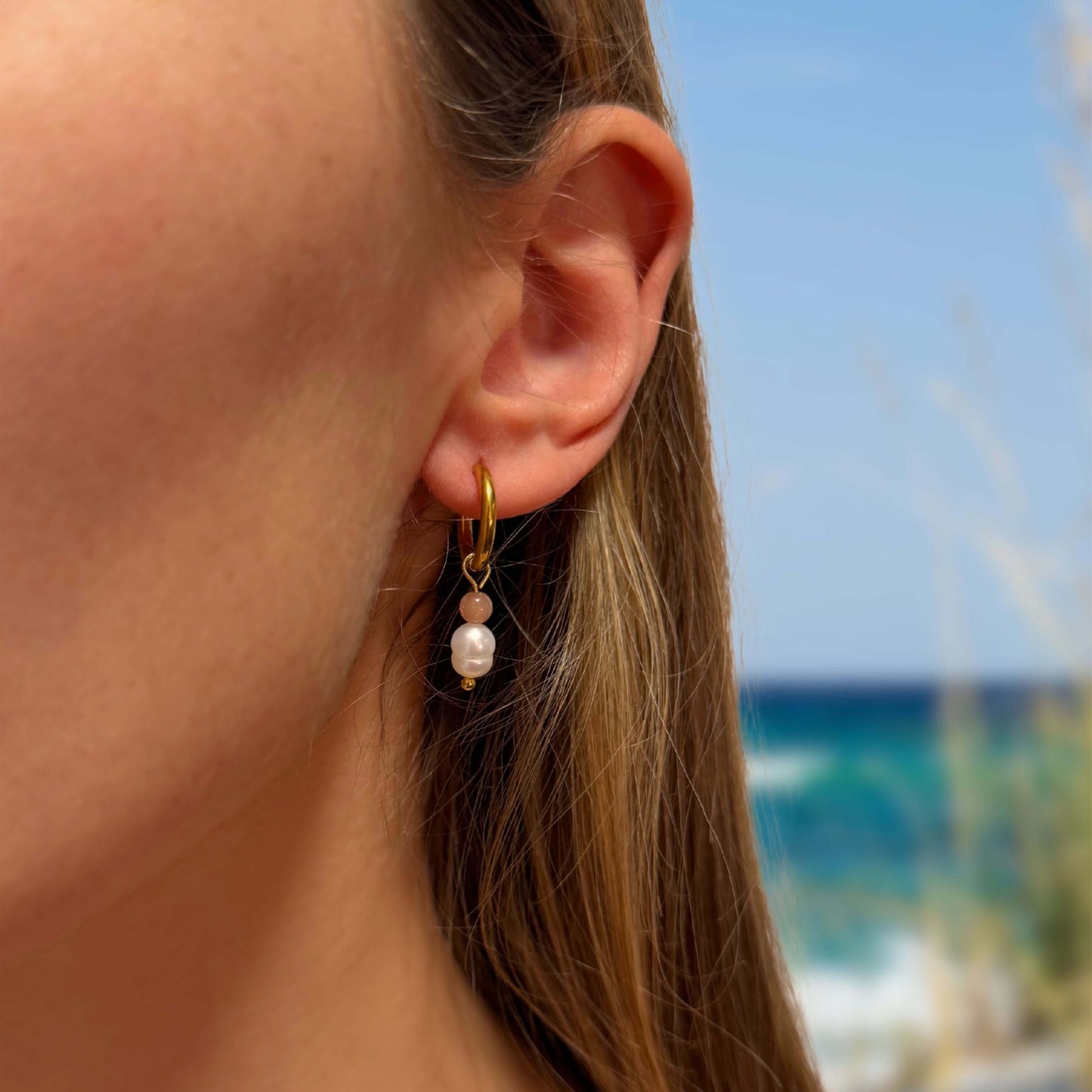 Boucles d'oreilles créoles en acier inoxydable avec perles d'eau douce porté par une femme sur la plage. 
