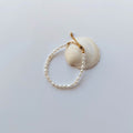 Bracelet en acier inoxydable doré orné de perles d’eau douce naturelles blanches, posé sur un coquillage, style délicat et élégant, sur fond neutre. 