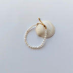 Bracelet en acier inoxydable doré orné de perles d’eau douce naturelles blanches, posé sur un coquillage, style délicat et élégant, sur fond neutre. 