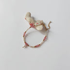Bracelet en quartz fraise et petites perles d'eau douce baroques entrecoupées de perles dorées en acier inoxydable, posé sur un morceau de corail blanc sur fond gris clair.