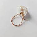 Bracelet Palythoa en perles d'eau douce baroques et pierres de quartz fraise alternées, entrecoupées de perles dorées en acier inoxydable, posé contre un coquillage blanc en spirale sur fond gris clair.
