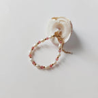 Bracelet Palythoa en perles d'eau douce baroques et pierres de quartz fraise alternées, entrecoupées de perles dorées en acier inoxydable, posé contre un coquillage blanc en spirale sur fond gris clair.