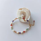 Bracelet en acier inoxydable, perles d'eau douce et pierres naturelles de couleur posé sur fond blanc et coquillages
