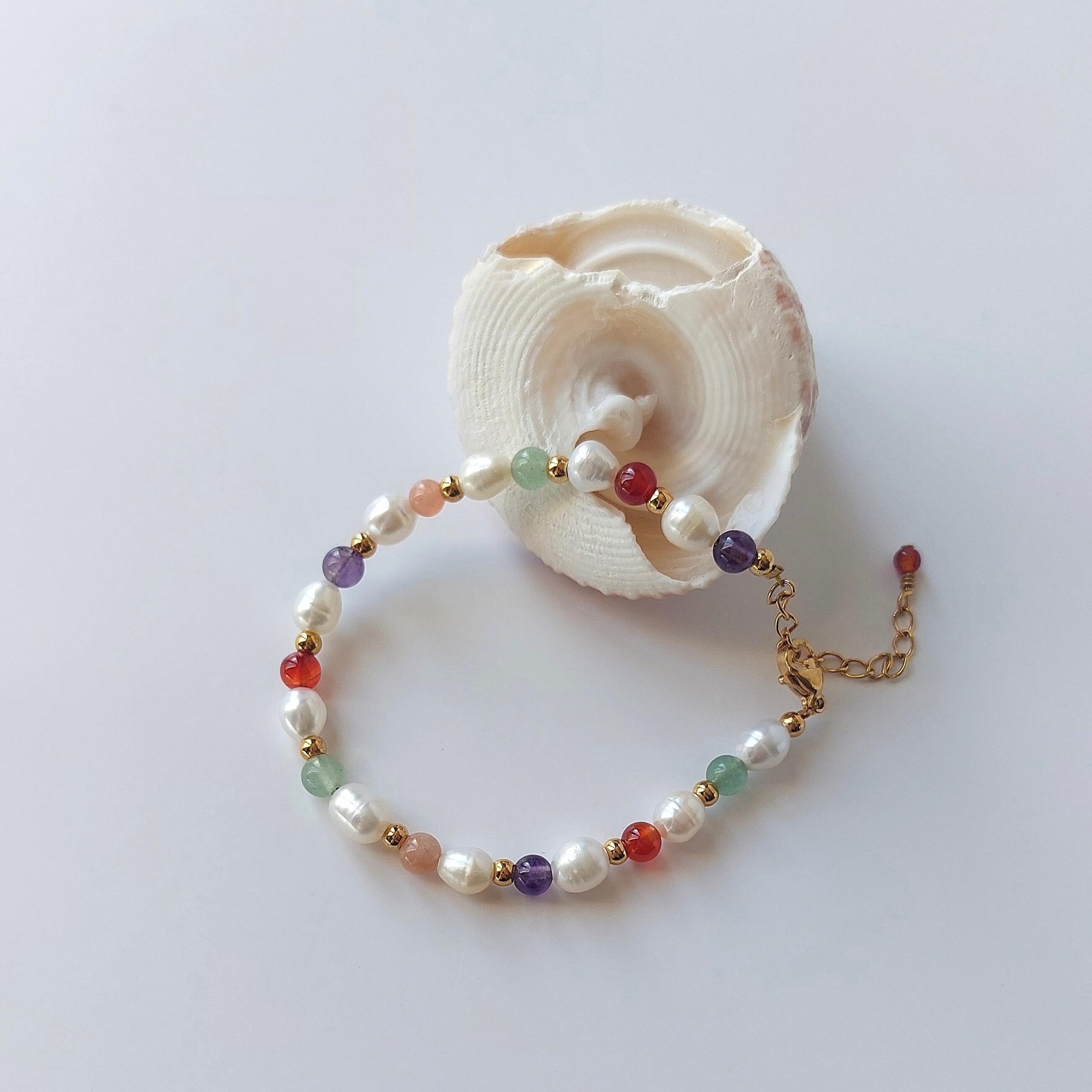 Bracelet en acier inoxydable, perles d'eau douce et pierres naturelles de couleur posé sur fond blanc et coquillages