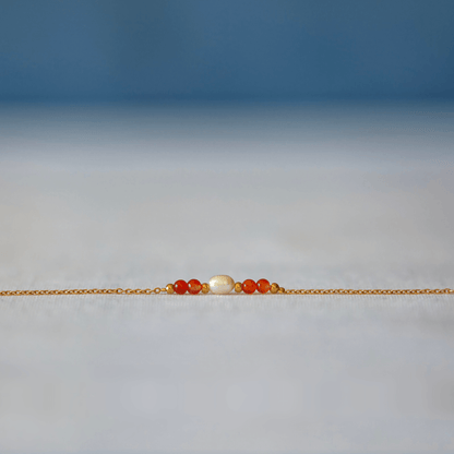 Bracelet élégant Acropora en perle d'eau douce et perles de cornaline orange posé sur fond gris.