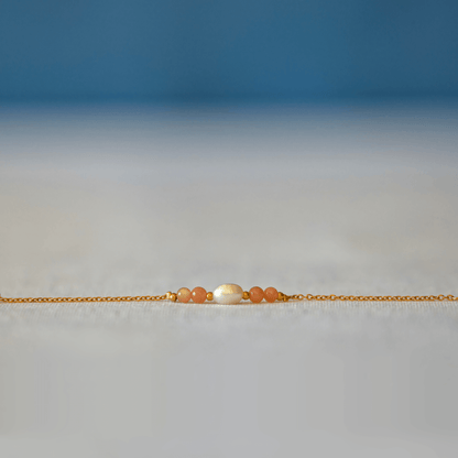 Bracelet élégant Acropora en perle d'eau douce et perles de pierre de soleil posé sur fond gris.