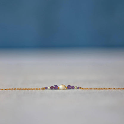 Bracelet Anthelia en perles d'eau douce et perles d'Améthyste violette posé sur fond gris.
