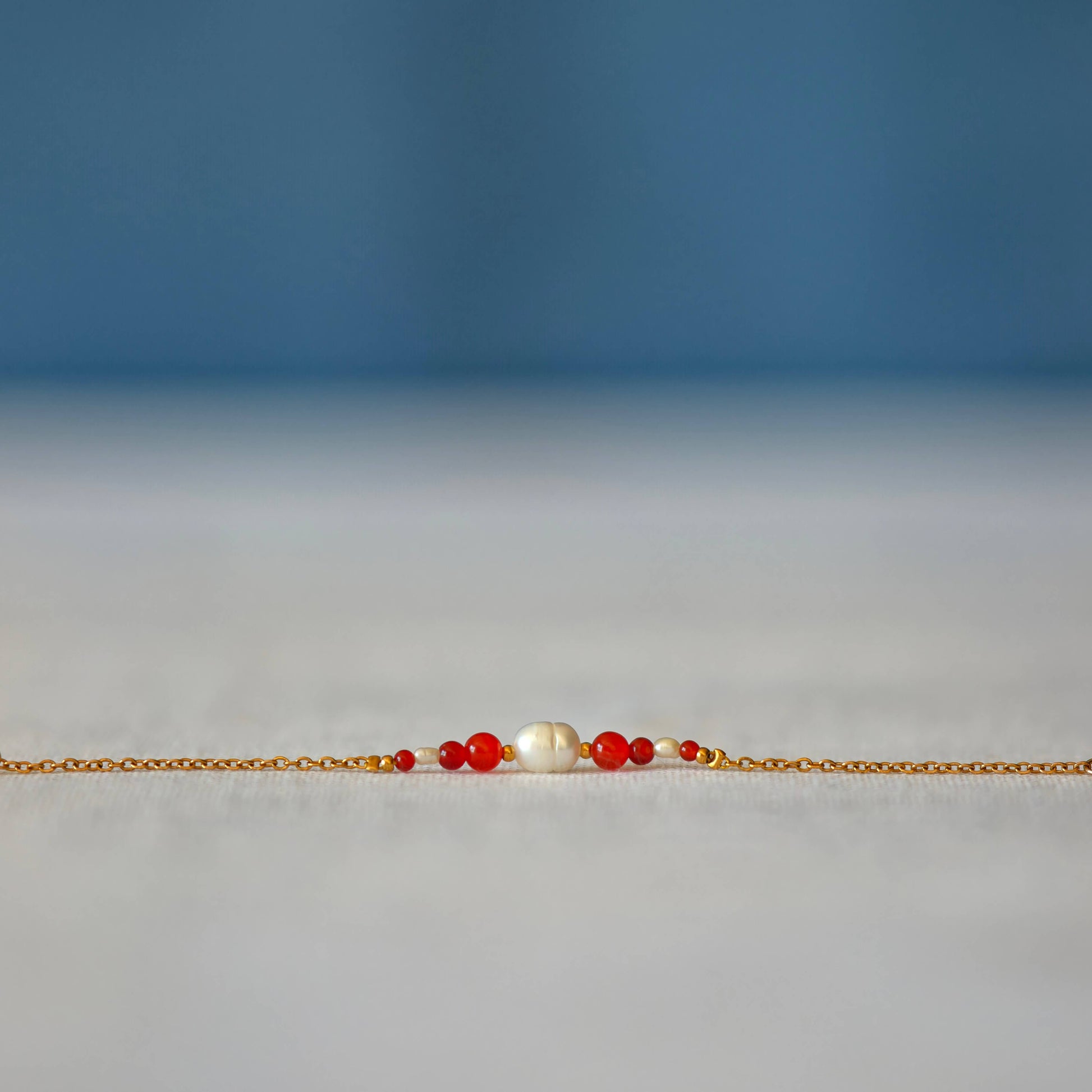 Bracelet Anthelia en perles d'eau douce et perles de cornaline rouge posé sur fond gris.