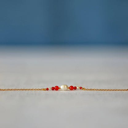 Bracelet Anthelia en perles d'eau douce et perles de cornaline rouge posé sur fond gris.