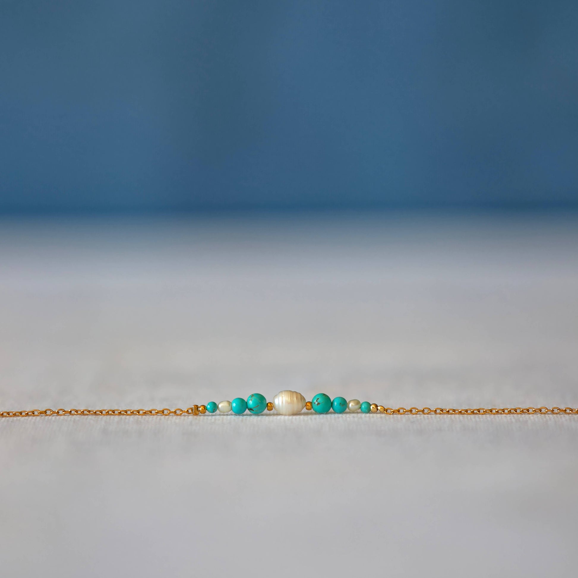 Bracelet Anthelia en perles d'eau douce et perles de turquoise bleue posé sur fond gris.