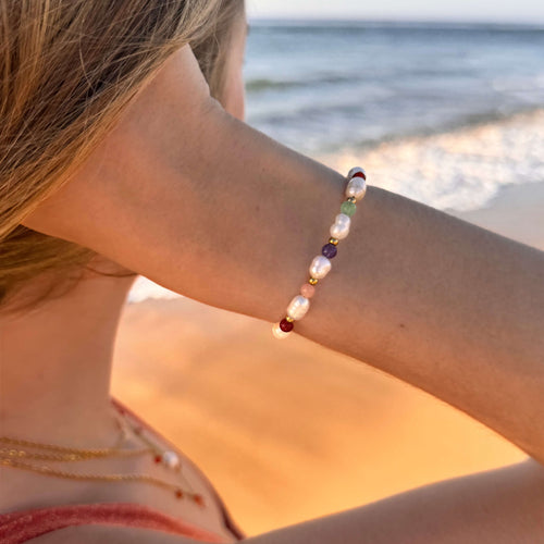 Bracelet en acier inoxydable doré avec perles d'eau douce et perles de couleur porté par une femme devant un coucher de soleil.