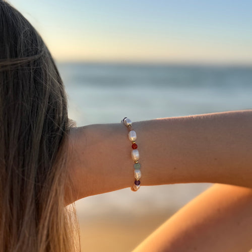 Bracelet en acier inoxydable avec perles d'eau douce et perles de couleur porté par une femme devant un coucher de soleil.