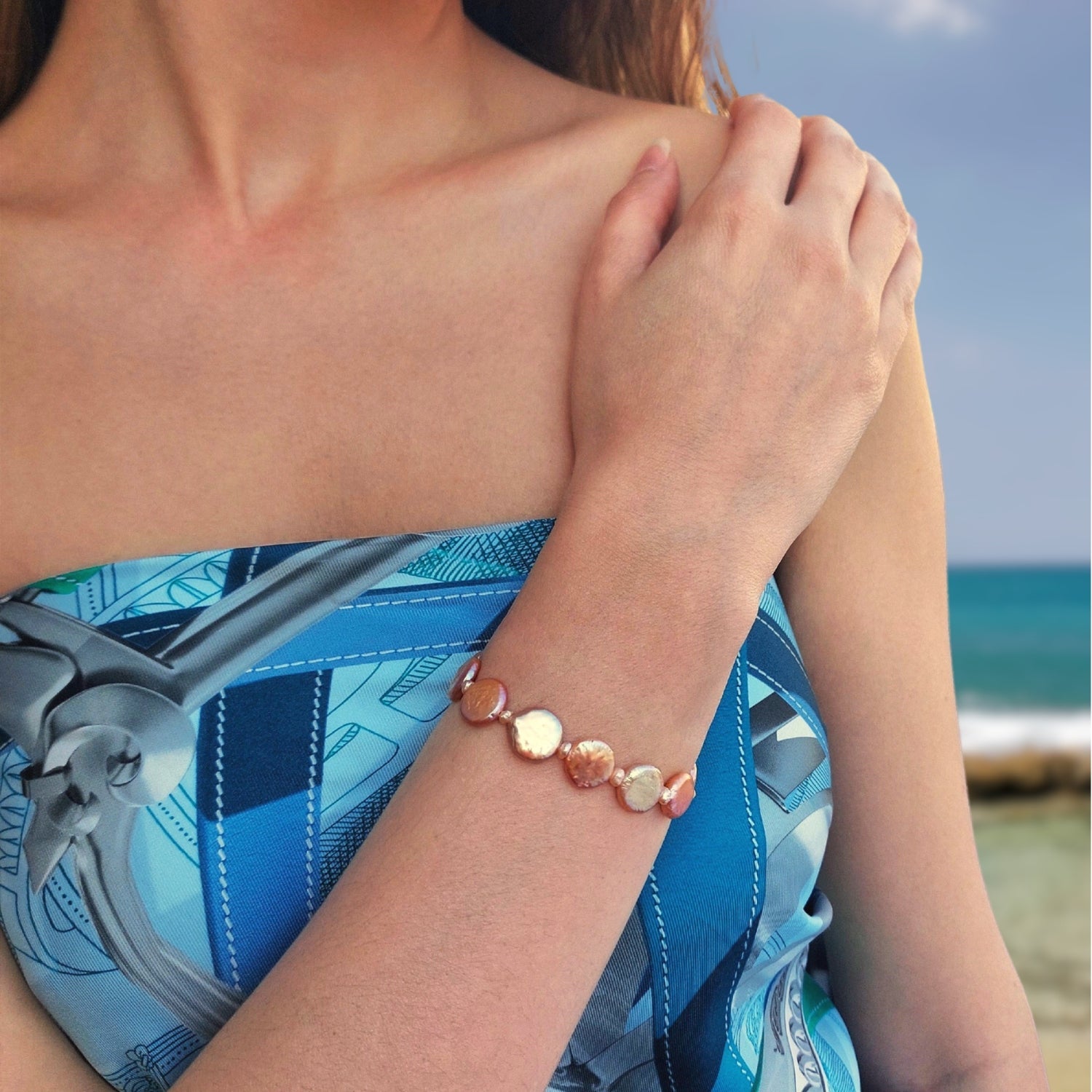 Bracelet en acier inoxydable doré avec perles d’eau douce naturelles oranges plates porté par une femme à la plage
