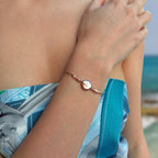 Bracelet en acier inoxydable doré avec perles d’eau douce naturelles violettes et perle centrale plate porté par une femme à la plage