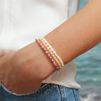 3 bracelets de perles d'eau douce blanches, oranges et violettes, portés en accumulation. 