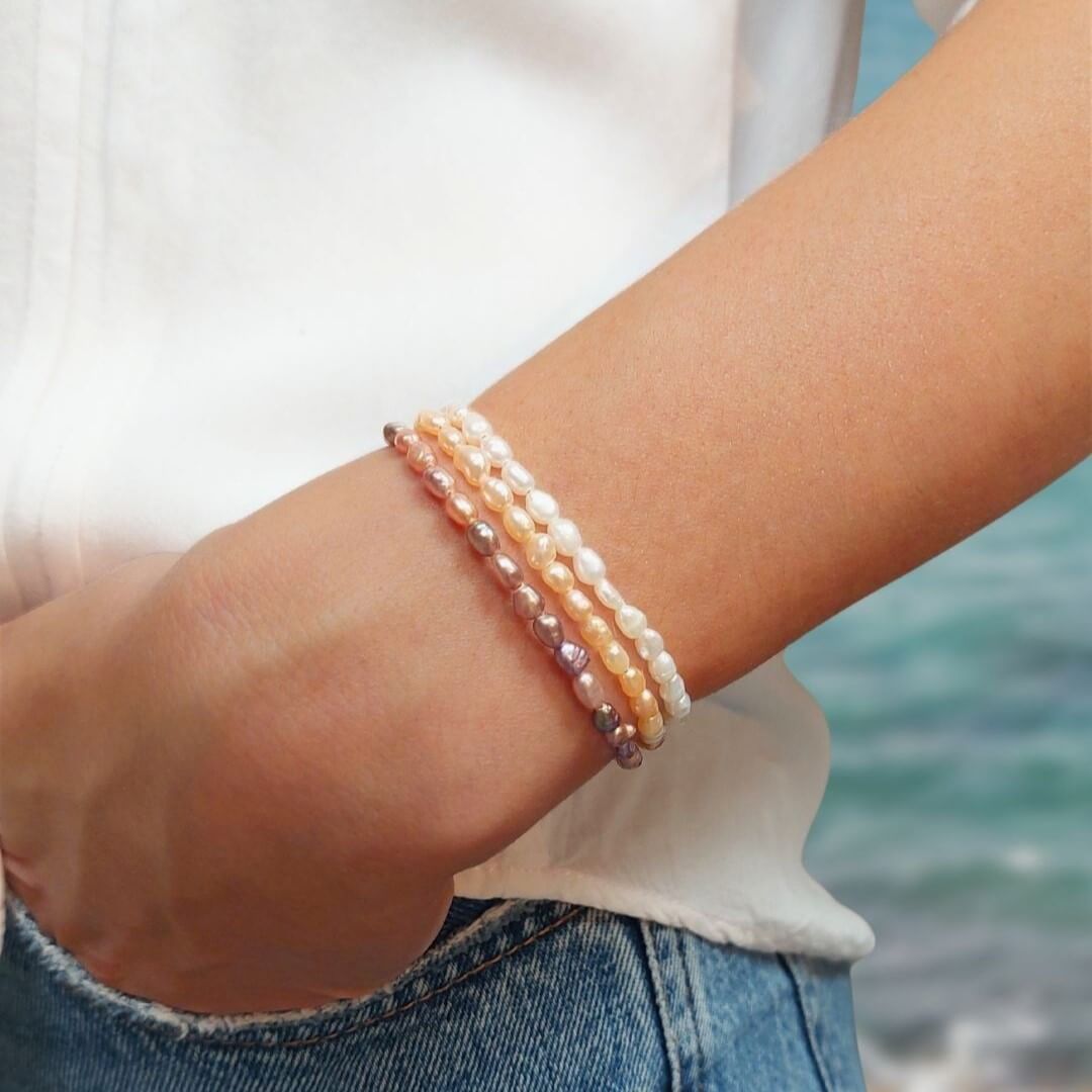 3 bracelets de perles d'eau douce blanches, oranges et violettes, portés en accumulation. 