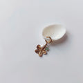 Charm à anneau ressort doré composé d'une perle d'eau douce blanche, d'une petite perle d'aventurine et d'un pendentif fleur à cinq pétales dorée texturée, posé contre un coquillage nacré blanc sur fond gris clair.