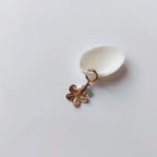 Charm à anneau ressort doré composé d'une perle d'eau douce blanche, d'une petite perle d'aventurine et d'un pendentif fleur à cinq pétales dorée texturée, posé contre un coquillage nacré blanc sur fond gris clair.
