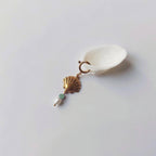 Charm à anneau ressort doré composé d'un pendentif coquille Saint-Jacques dorée striée, d'une petite perle d'aventurine et d'une perle d'eau douce blanche baroque, posé contre un coquillage nacré blanc sur fond gris clair.