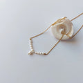 Collier Aurea en acier inoxydable doré avec perles d’eau douce naturelles blanches, bijou fin et élégant posé sur un coquillage, sur fond neutre.