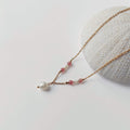 Collier Euphyllia en quartz fraise et petites perles d'eau douce sur fine chaîne dorée en acier inoxydable, avec une perle d'eau douce baroque en pendentif, posé contre un oursin blanc sur fond gris clair.