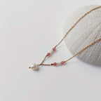 Collier Euphyllia en quartz fraise et petites perles d'eau douce sur fine chaîne dorée en acier inoxydable, avec une perle d'eau douce baroque en pendentif, posé contre un oursin blanc sur fond gris clair.