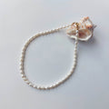 Collier ras de cou orné de perles d’eau douce blanches, présenté à la lumière naturelle sur un coquillage et un fond neutre.