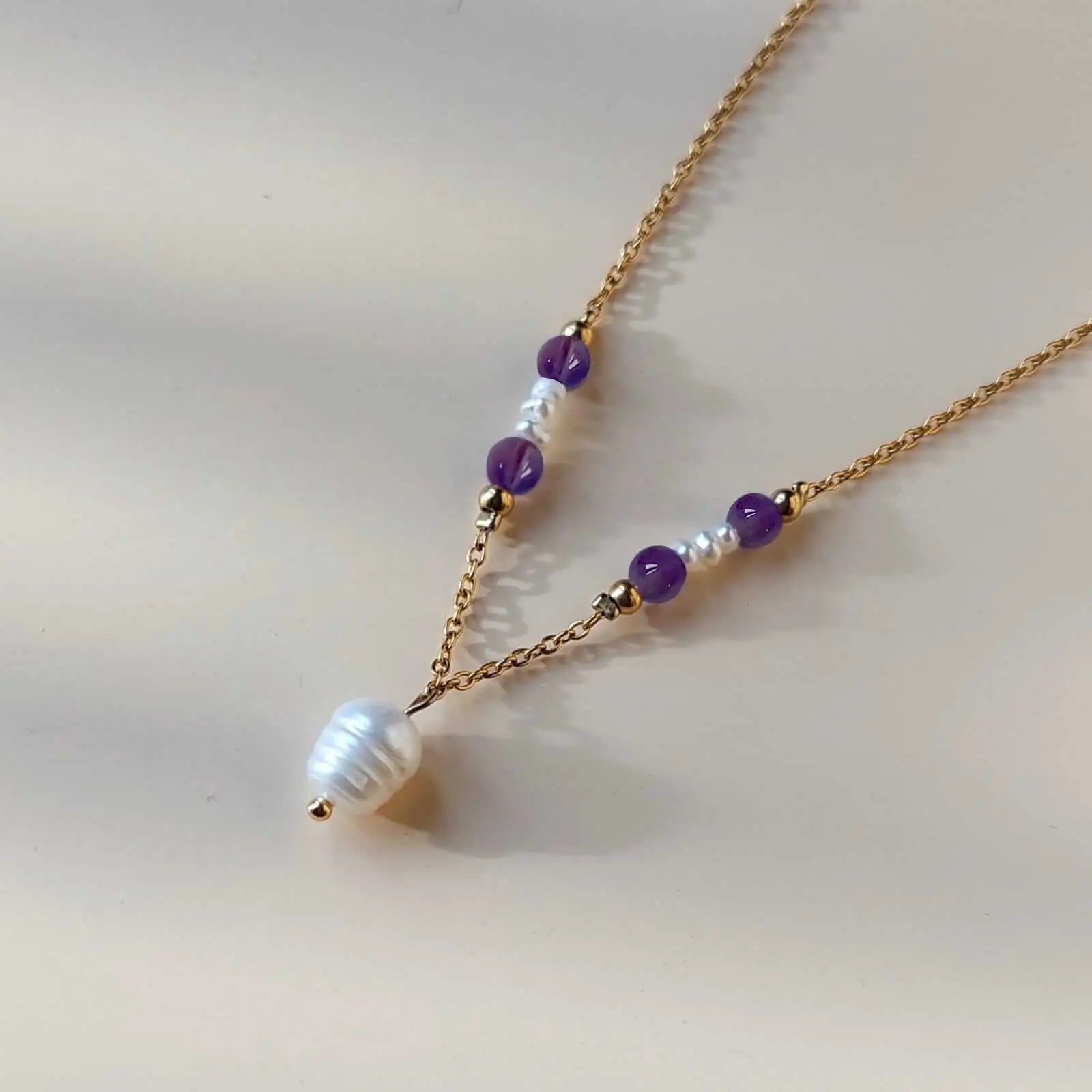 Collier pendentif en acier inoxydable avec perle d'eau douce centrale et pierres d'améthyste violettes, créant un effet délicat et harmonieux.
