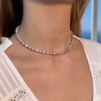 Collier ras de cou en perles d’eau douce naturelles violettes, porté par une femme, avec un fond bleu ciel flouté.