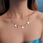 Collier en acier inoxydable doré avec perles d’eau douce plates et petits trios de perles blanches porté par une femme à la plage