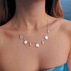 Collier en acier inoxydable argenté avec perles d’eau douce plates et petits trios de perles blanches porté par une femme à la plage
