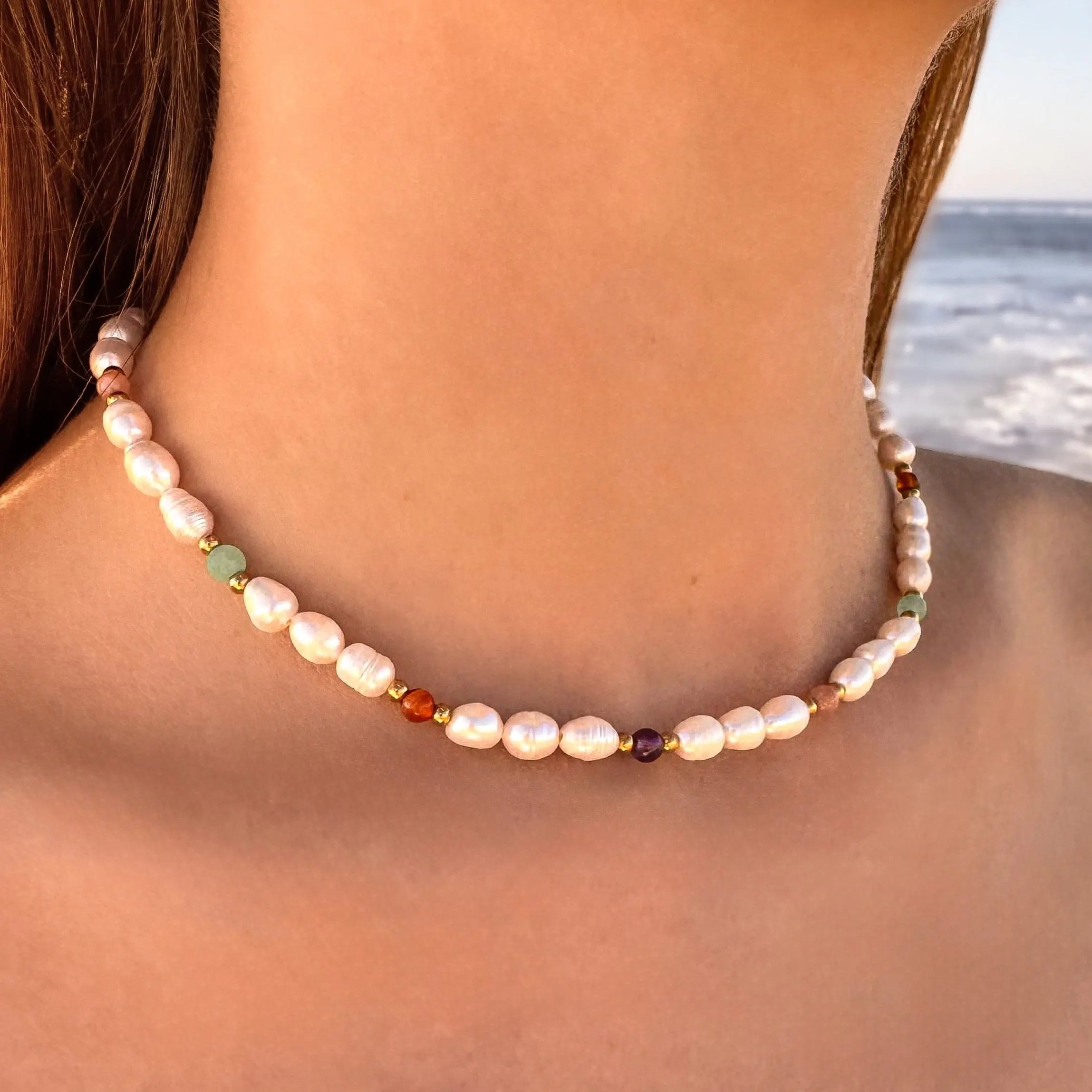 Collier ras de cou en acier inoxydable avec perles d'eau douce et perles de couleur porté par une femme à la plage.