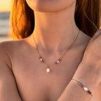 Collier pendentif en acier inoxydable avec perles d'eau douce et perles de couleur porté par une femme devant l'océan.