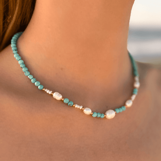 Collier ras de cou en acier inoxydable avec perles d'eau douce et perles de couleur porté par une femme bronzée à la plage.