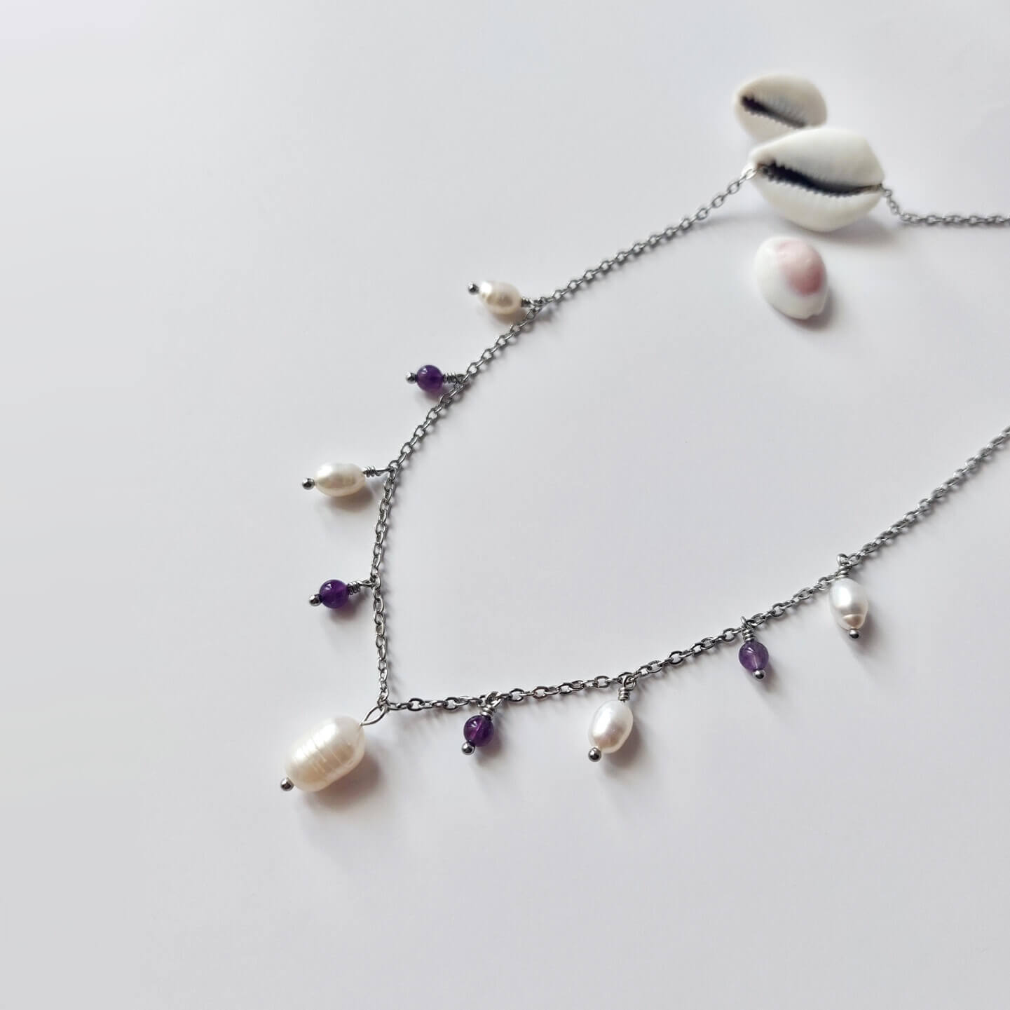 Collier Meandrina en acier inoxydable argenté, perles d'eau douce et perles d'améthyste violettes posé sur fond blanc