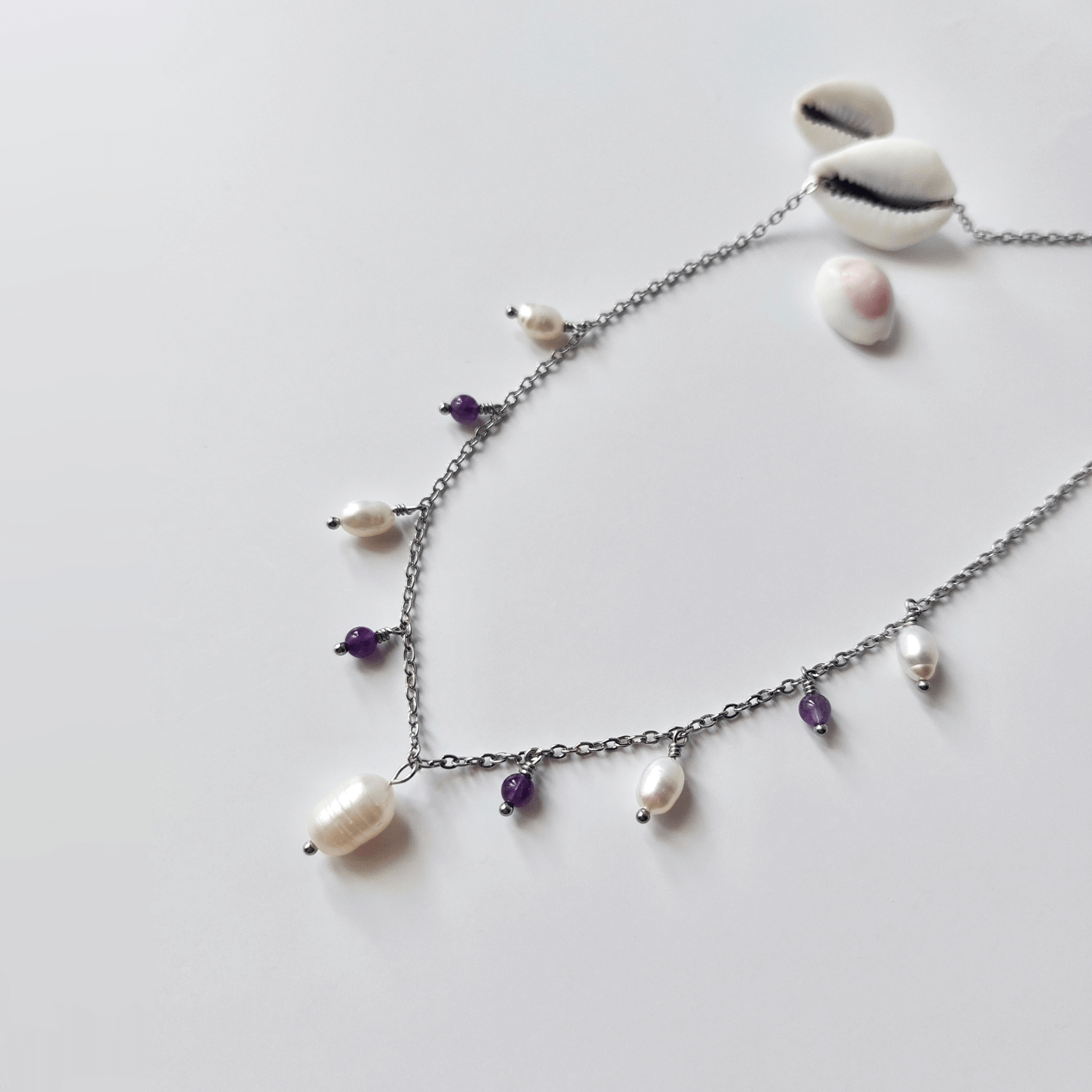 Collier Meandrina en acier inoxydable argenté, perles d'eau douce et perles d'améthyste violettes posé sur fond blanc