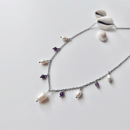 Collier Meandrina en acier inoxydable argenté, perles d'eau douce et perles d'améthyste violettes posé sur fond blanc