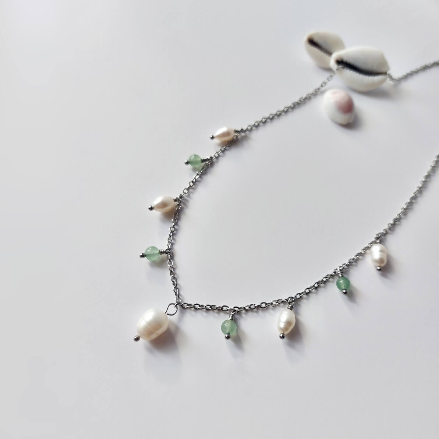 Collier Meandrina en acier inoxydable argenté, perles d'eau douce et perles d'aventurine vertes posé sur fond blanc