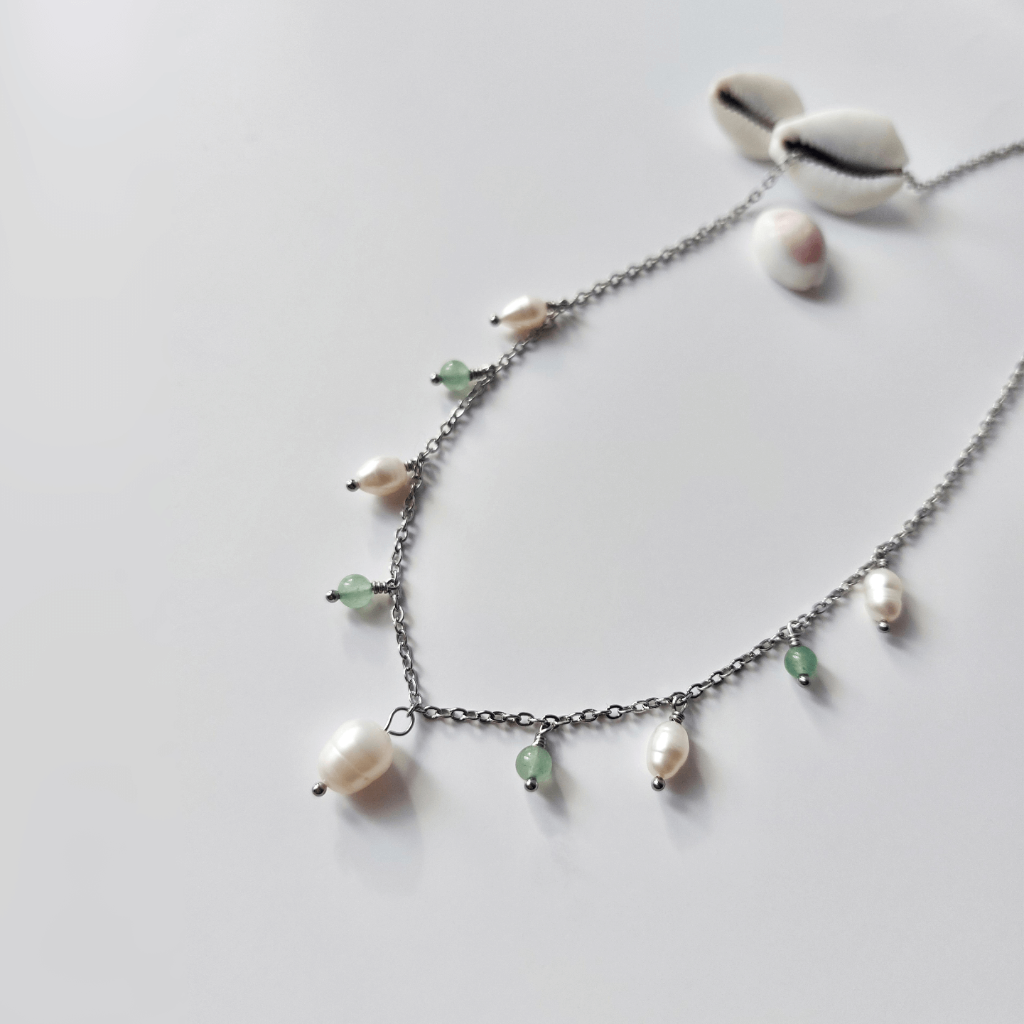 Collier Meandrina en acier inoxydable argenté, perles d'eau douce et perles d'aventurine vertes posé sur fond blanc