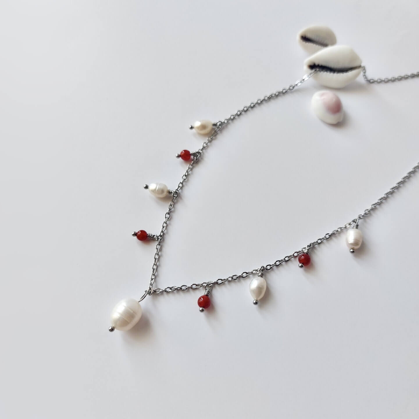 Collier Meandrina en acier inoxydable argenté, perles d'eau douce et perles de cornaline rouge posé sur fond blanc