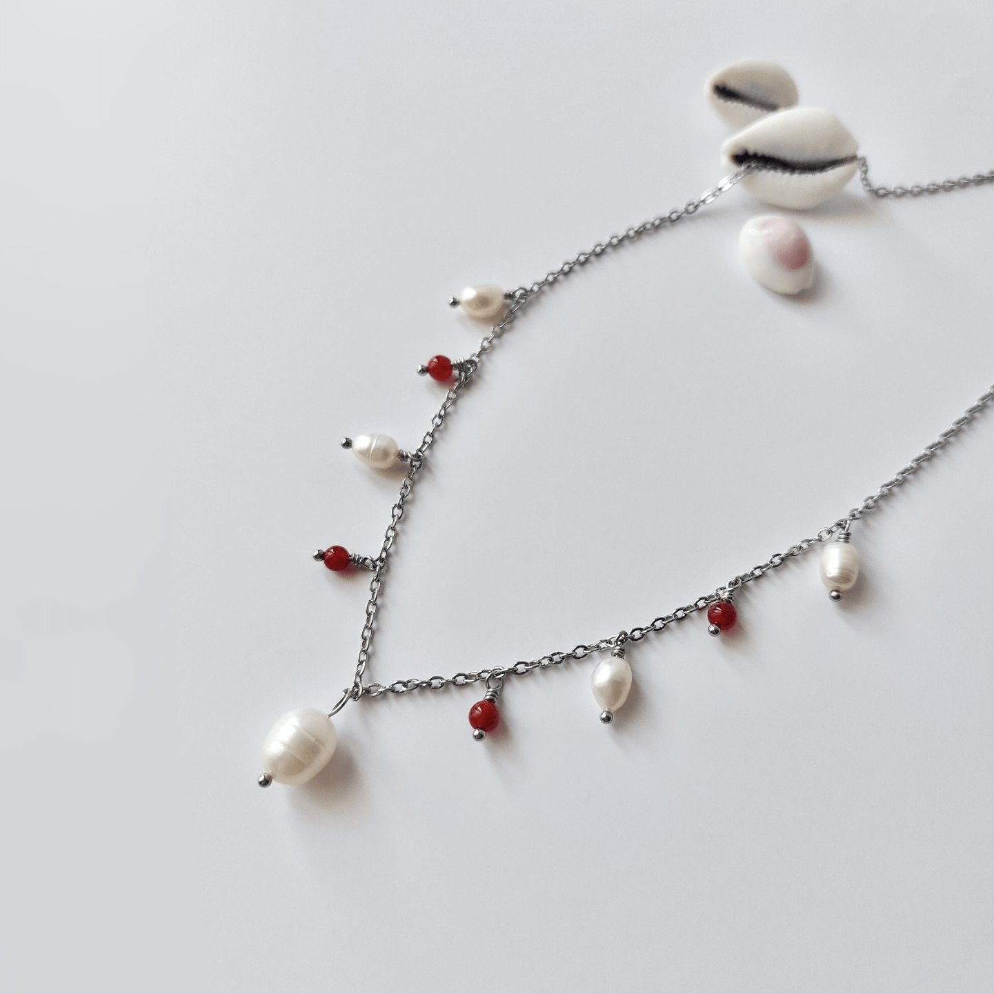 Collier Meandrina en acier inoxydable argenté, perles d'eau douce et perles de cornaline rouge posé sur fond blanc